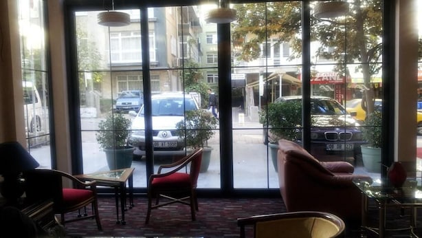 Un hall d’hôtel avec de grandes fenêtres, une table en verre et des chaises rouges.