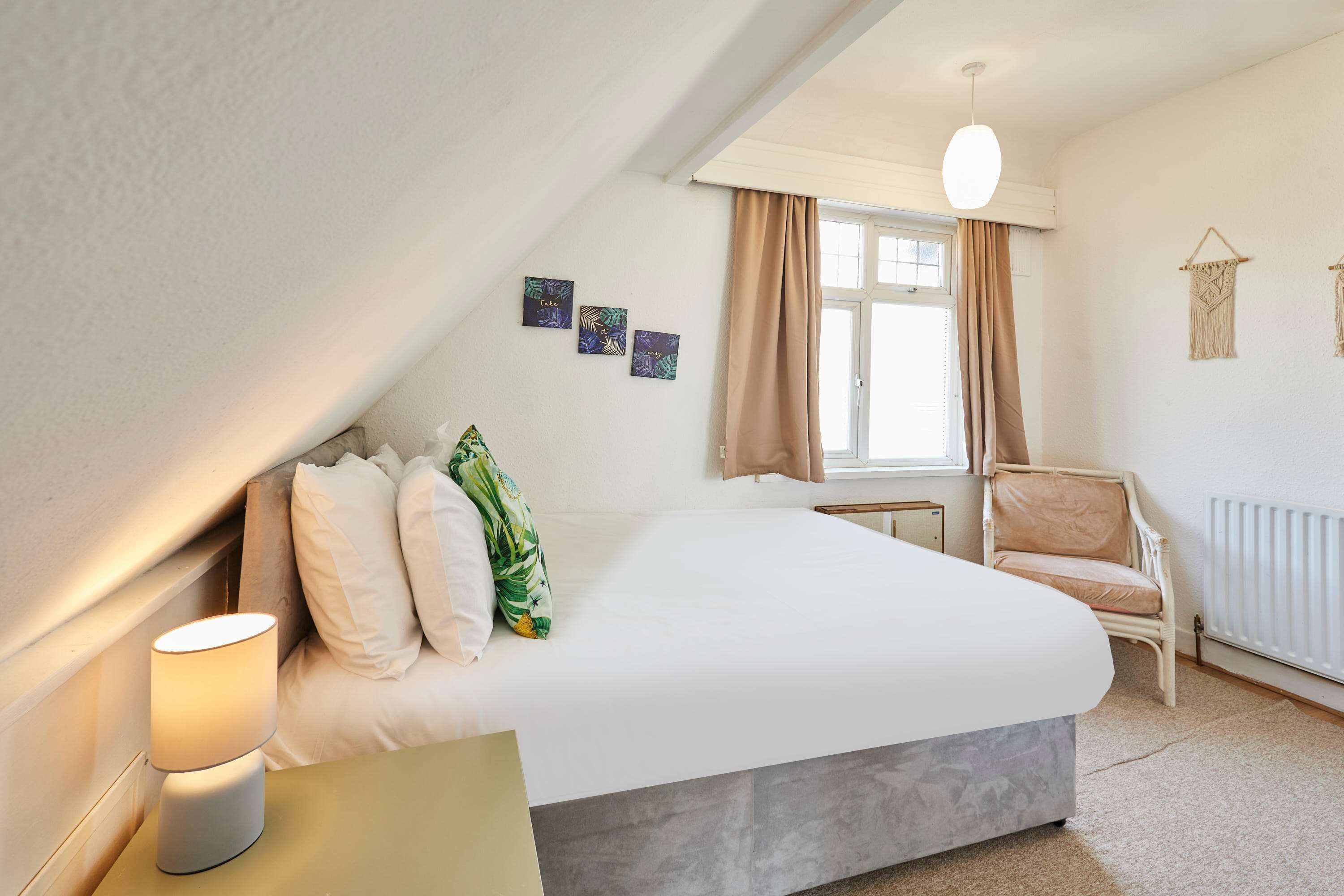 A bedroom with a bed, a nightstand, a chair, and a window with curtains.