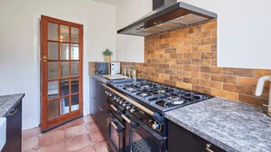 A kitchen with a gas stove, oven, and a brick backsplash. - Host Stay The Midland Nest (Birmingham)