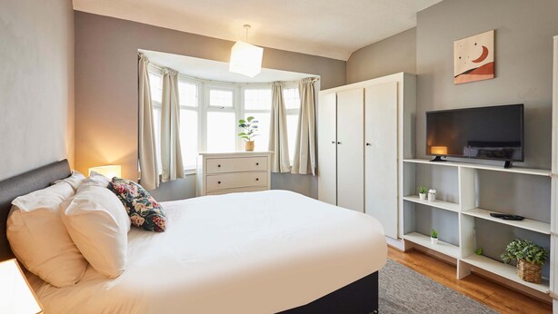 A bedroom with a large bed, a TV, a wardrobe, and a window with curtains. - Host Stay The Midland Nest (Birmingham)