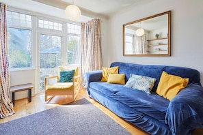 A room with a blue sofa, a wooden chair, a bench, and a large window with curtains. - Host Stay The Midland Nest (Birmingham)