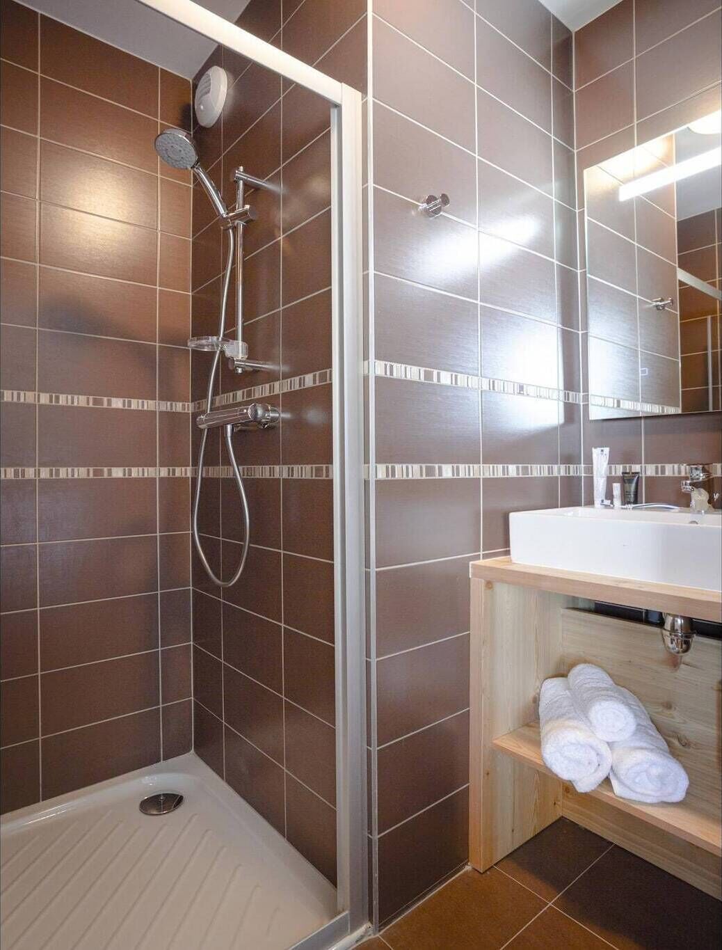 Un bagno moderno con doccia, lavandino e mensola in legno con asciugamani.