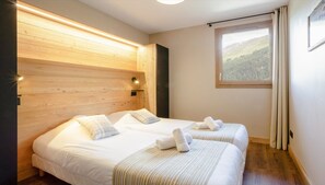 Camera d'albergo con due letti, testiera in legno, una finestra vista foresta e una lampada a soffitto.
