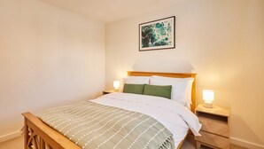 Een netjes opgemaakt bed met een houten hoofdeinde, twee nachtkastjes met lampen en een ingelijste afbeelding aan de muur.