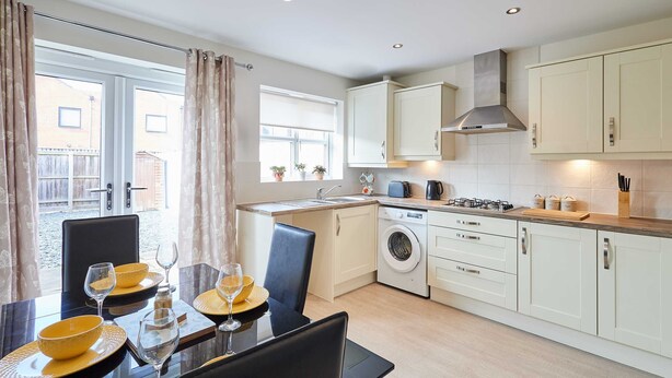 Een moderne keuken met een eethoek, inclusief een tafel gedekt voor twee personen met wijnglazen en kommen, een wasmachine en een fornuis.