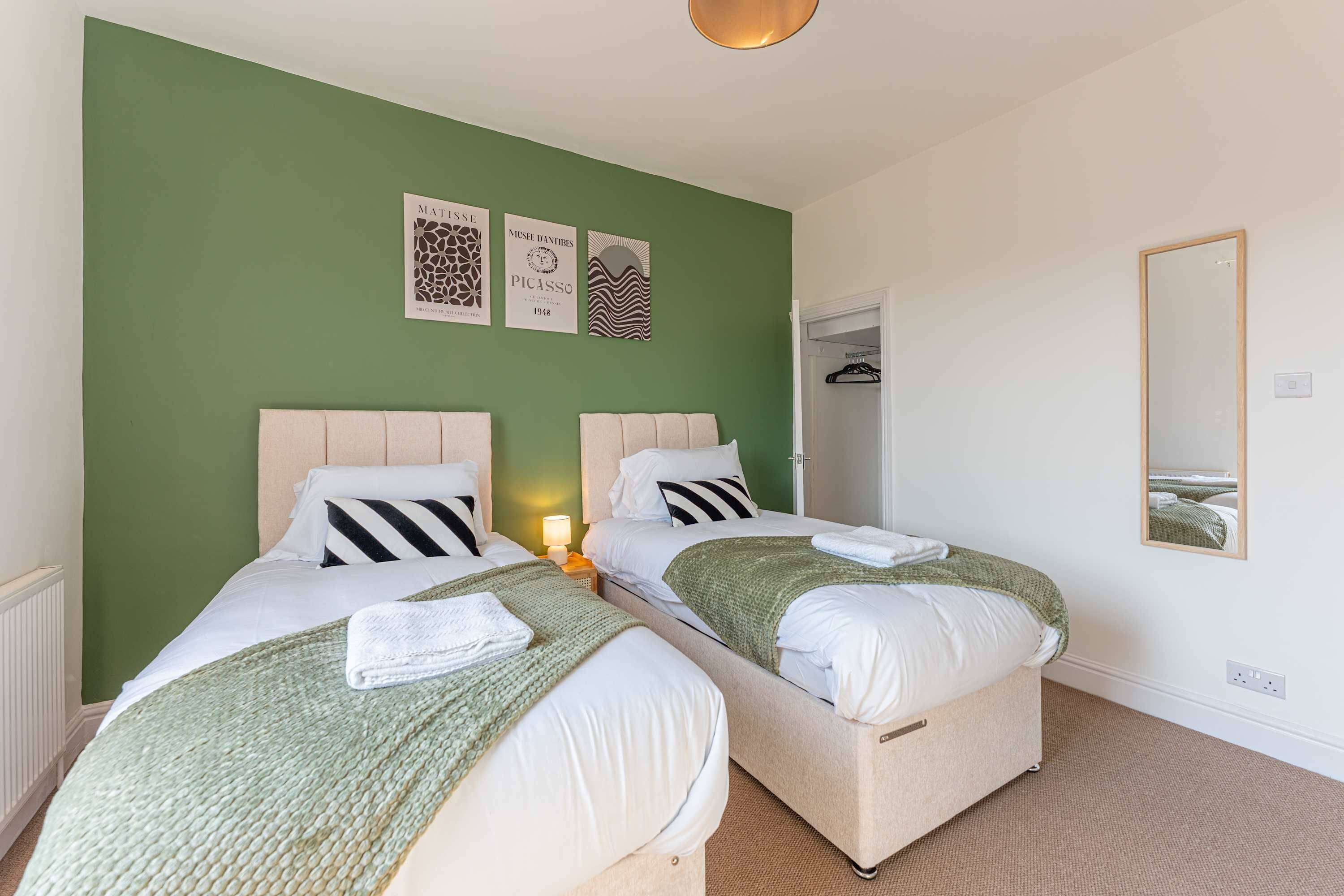 A bedroom with two beds, green walls, and artwork.