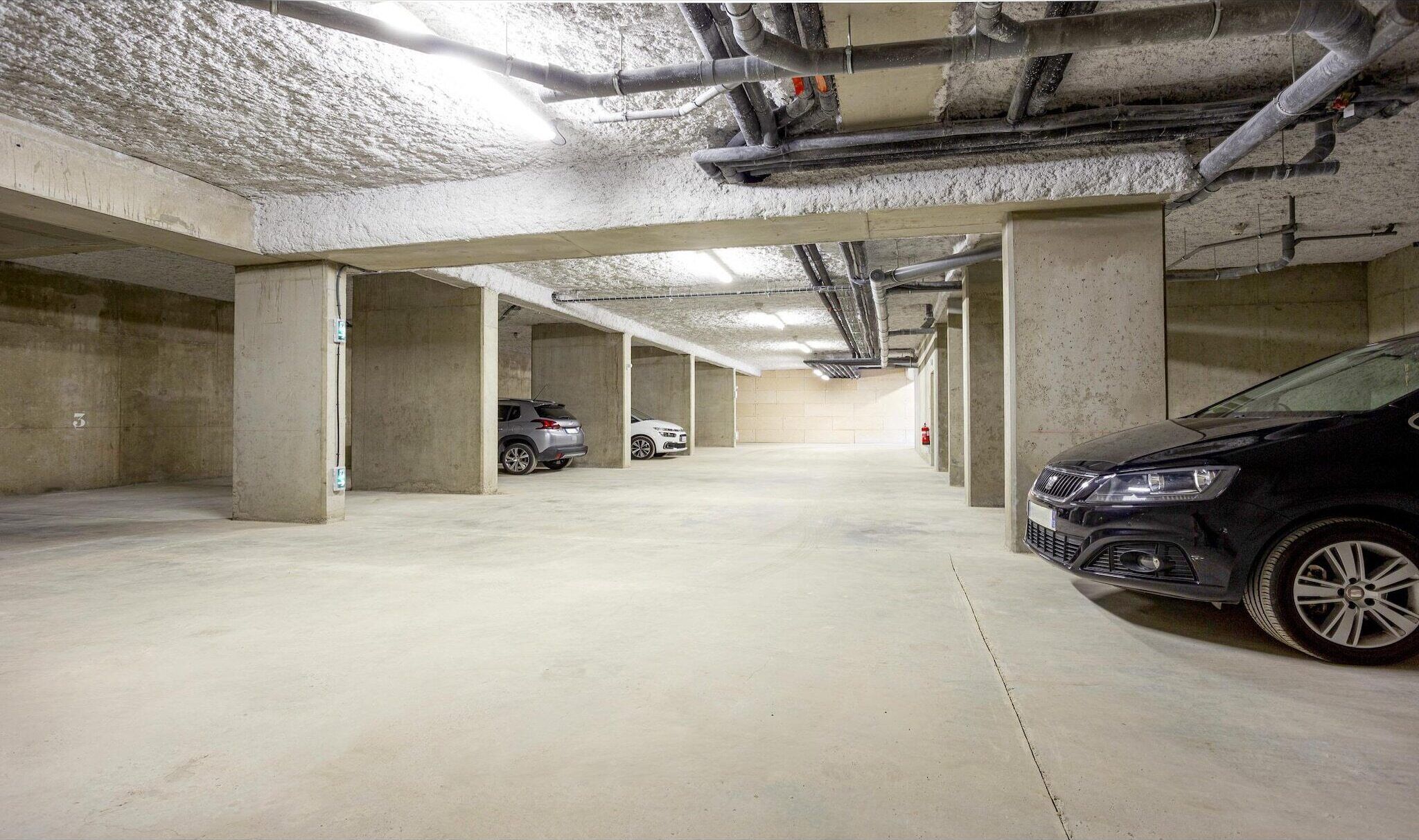 A multi-level underground parking garage with concrete pillars and overhead pipes.
