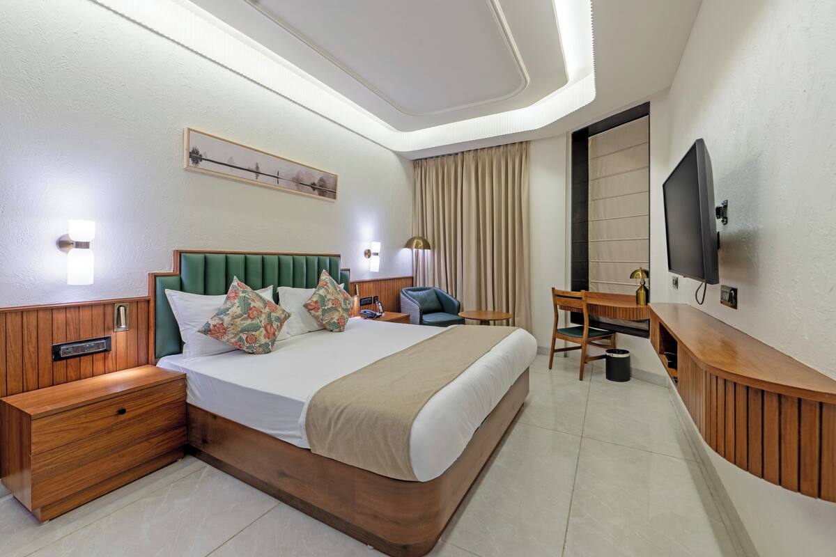 A hotel room with a large bed, a desk, a chair, a TV, and a nightstand.
