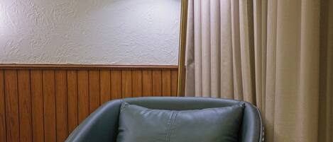 A room with a wooden panel wall, a green leather chair, a round wooden table, and a floor lamp.
