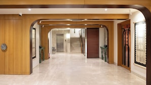 A spacious hallway with a wooden door on the left, a staircase in the center, and a large wooden door on the right. - Hotel Idyllic Inn (Bhopal)