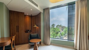 A modern room with a wooden cabinet, a dining table, a chair, a small round table, and a large window with curtains. - Hotel Idyllic Inn (Bhopal)