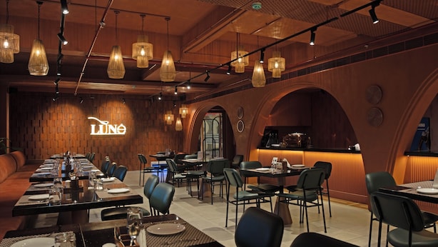 A restaurant with a long communal table, individual tables, and hanging lights. - Hotel Idyllic Inn (Bhopal)