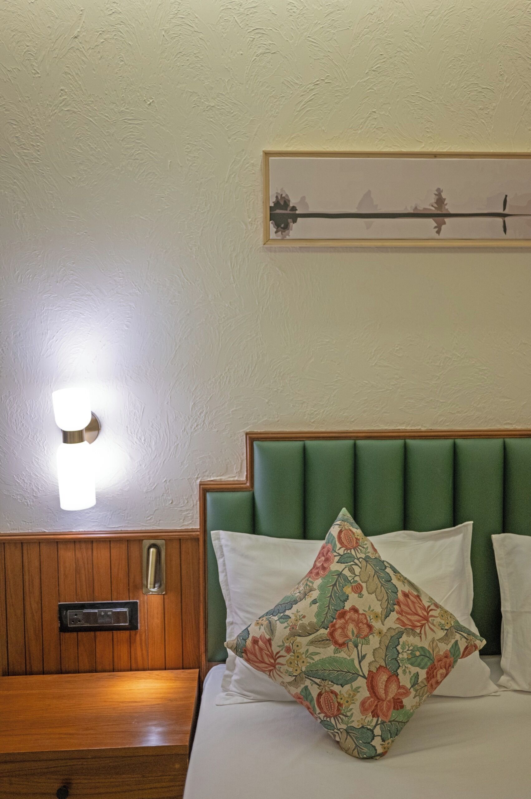 Ein Hotelzimmer mit einem Nachttisch aus Holz, einem grünen, gepolsterten Kopfteil und einem blumigen Kopfkissen.