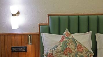 A hotel room with a wooden nightstand, a green upholstered headboard, and a floral pillow.