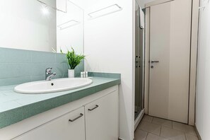 Ein modernes Badezimmer mit einem weißen Waschbecken, einer grünen Arbeitsplatte und einer Topfpflanze.