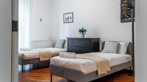 A modern bedroom with two single beds, a dark dresser, a potted plant, and a framed picture on the wall. - Marvellous 2BR flat near city centre (Milan)