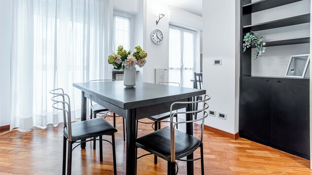 A modern dining area with a dark table, black chairs, and a vase of flowers. - Marvellous 2BR flat near city centre (Milan)