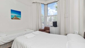 A hotel room with two beds, a TV, a chair, and a painting of a beach scene. - Amhurst Hotel (London)