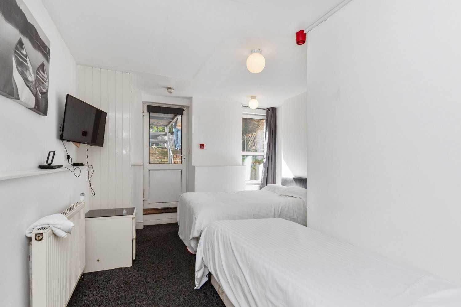 Habitación de hotel con dos camas individuales, un televisor montado en la pared, un escritorio con una silla y una ventana con vistas al exterior.