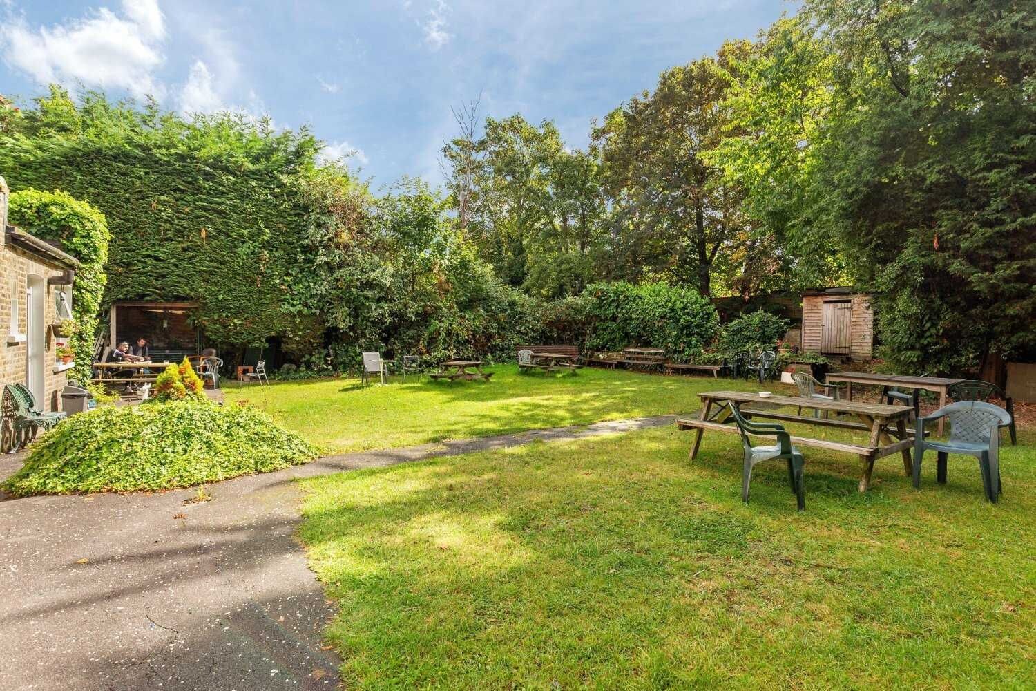 A garden with picnic tables and chairs, a brick building, and a wooden shed.