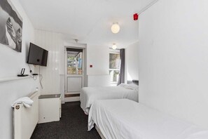 Habitación de hotel con dos camas individuales, un televisor montado en la pared, un escritorio con una silla y una ventana con vistas al exterior.