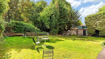 A backyard with picnic tables and benches, surrounded by dense trees and a wooden structure.