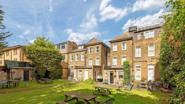 A courtyard with multiple buildings, outdoor seating, and a large tree. - Amhurst Hotel (London)