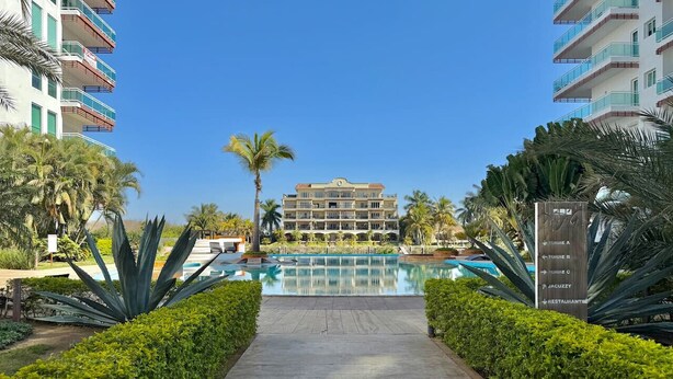 Un resort con piscina central, rodeado de setos cuidados y palmeras.
