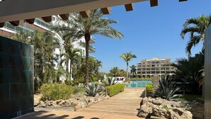 Un camino en un resort que lleva a una piscina, con palmeras y un edificio al fondo.