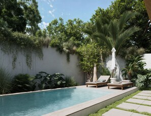 A swimming pool with lounge chairs and a white umbrella, surrounded by lush greenery and a white wall.