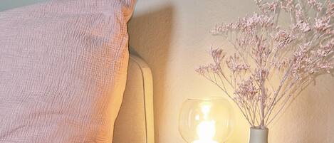 A cozy corner with a wooden side table, a white vase with dried flowers, and a lit table lamp.