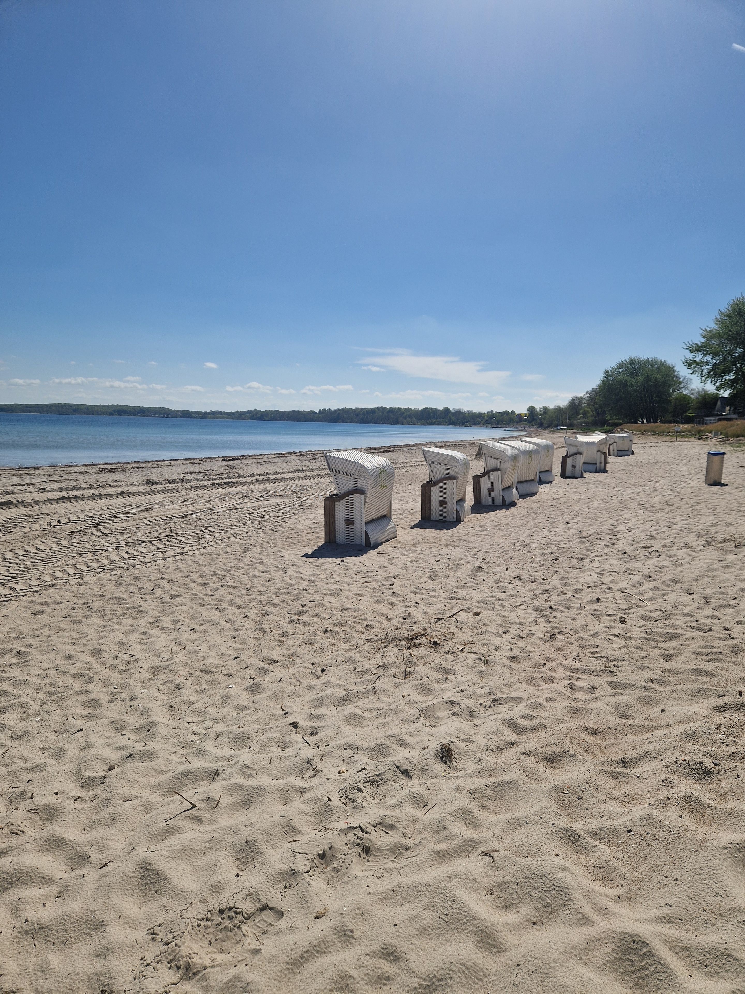 Ein Sandstrand mit Reihen weißer Liegestühle und blauem, wolkenlosem Himmel.
