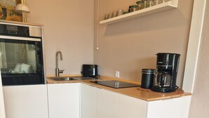 Cocina compacta con armarios blancos, encimera de madera, un lavabo, estufa y cafetera.