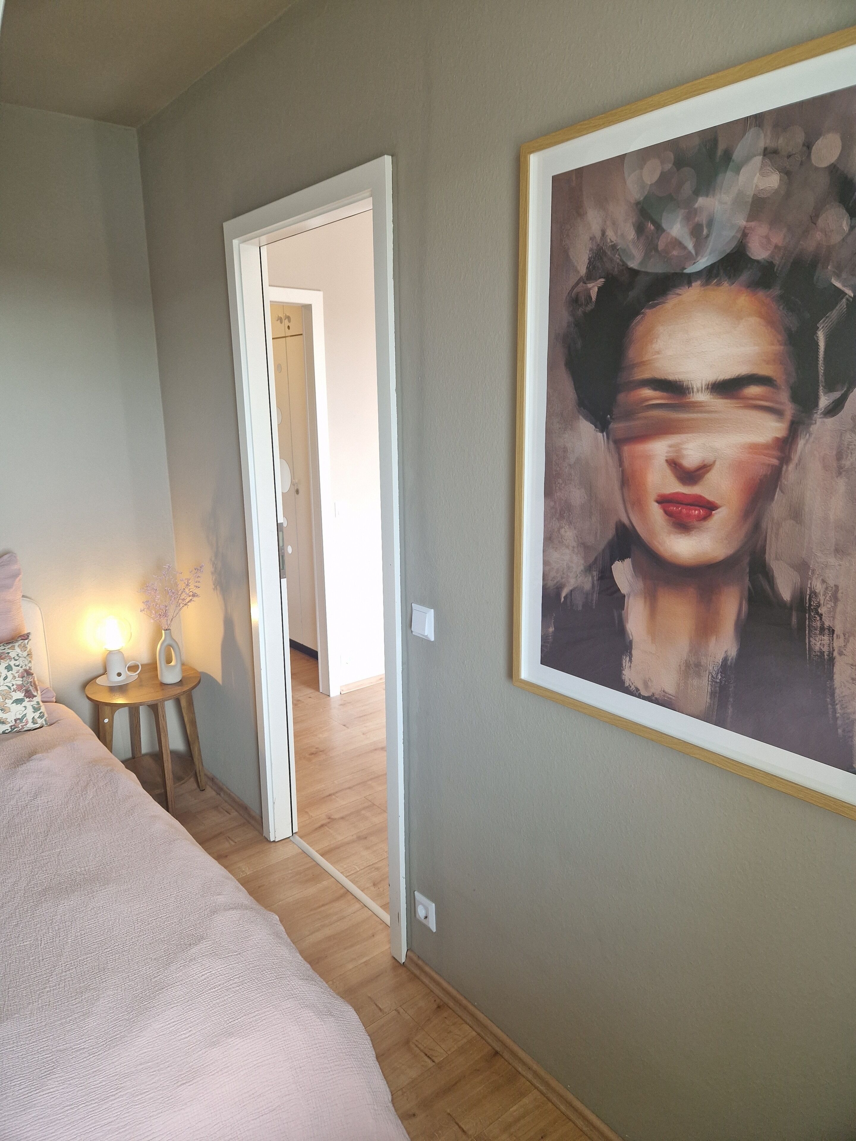 Een slaapkamer met een bed, nachtkastje en een schilderij aan de muur.