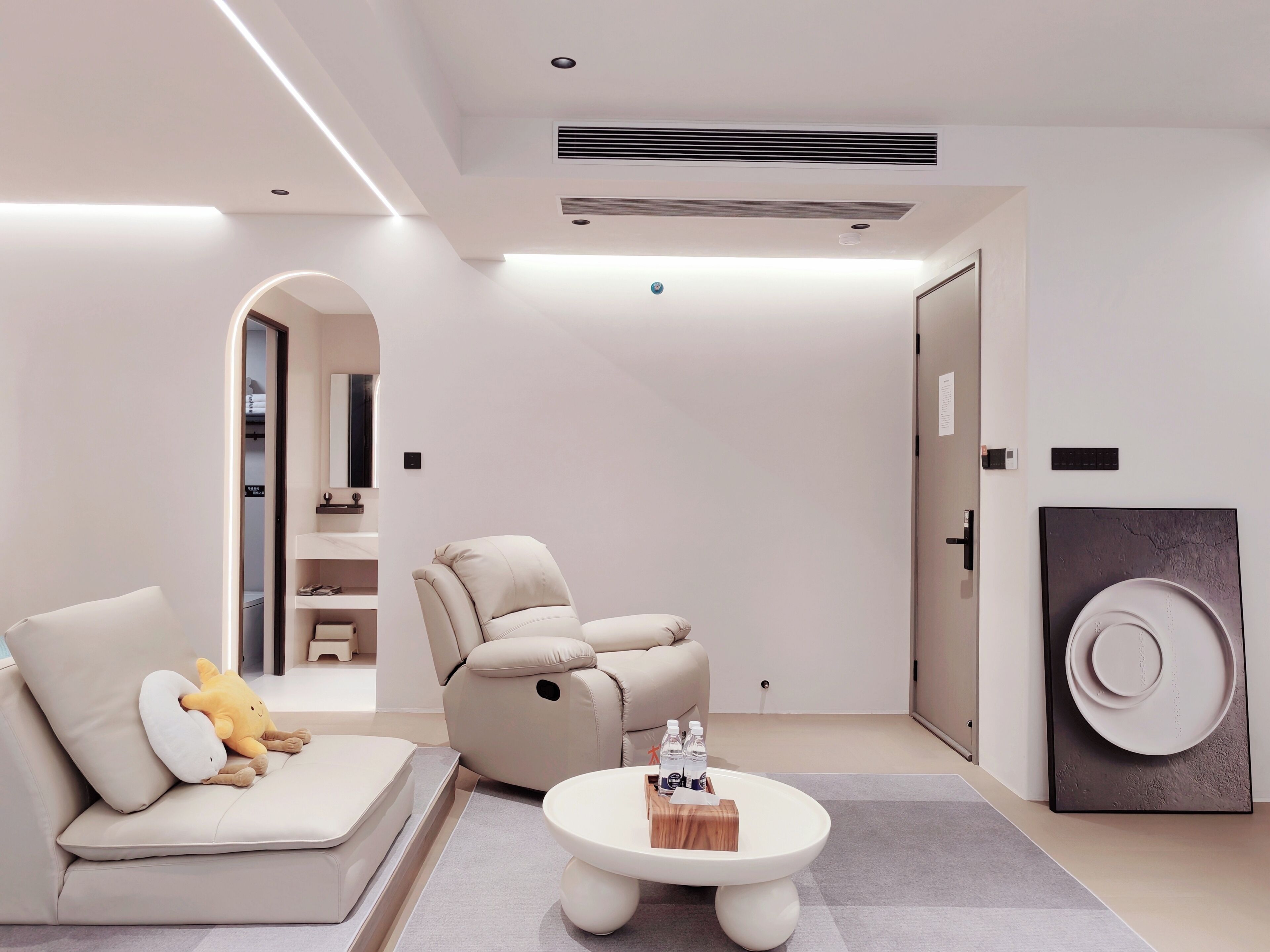 A modern living room with a sofa, a recliner, a coffee table, and a door with a textured artwork.