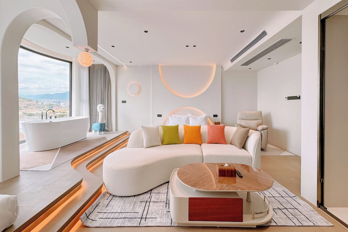 A modern living room with a curved sofa, a round coffee table, and a view of a cityscape through large windows.