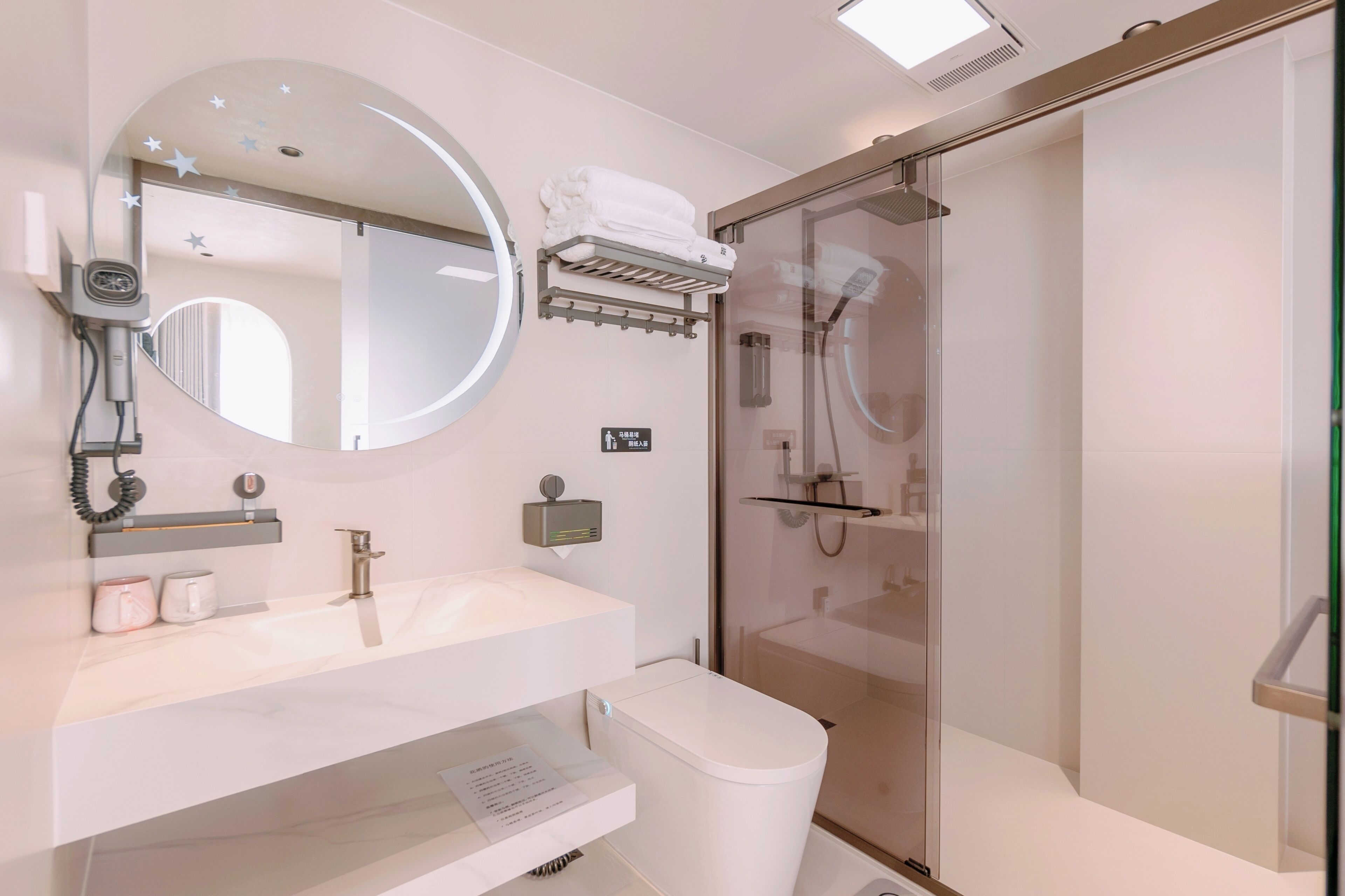 A modern bathroom with a round mirror, a toilet, a glass-enclosed shower, and a towel rack.