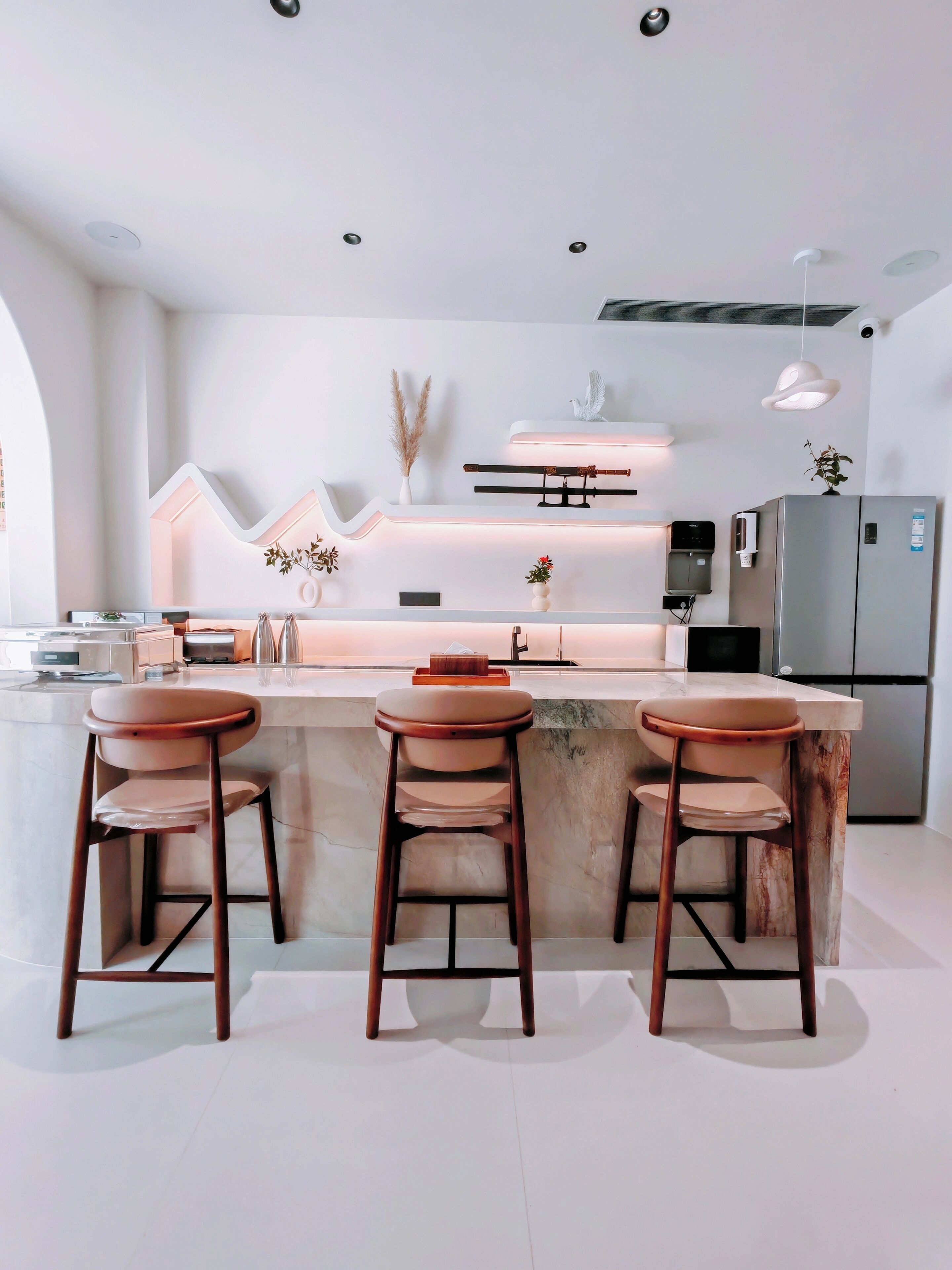 A modern kitchen with a central island, bar stools, a refrigerator, and pendant lighting.