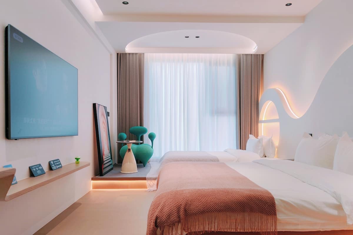 A modern hotel room with a large bed, a small table, a chair, and a TV mounted on the wall.