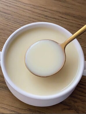A white cup with a gold spoon filled with a clear liquid, placed on a wooden surface.