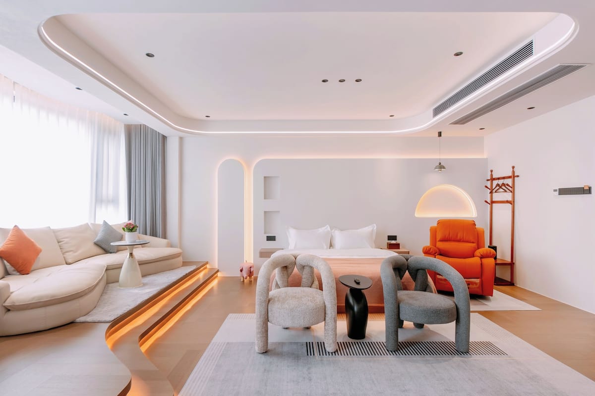 A modern hotel room with a curved ceiling, a sofa, a bed, and two chairs.