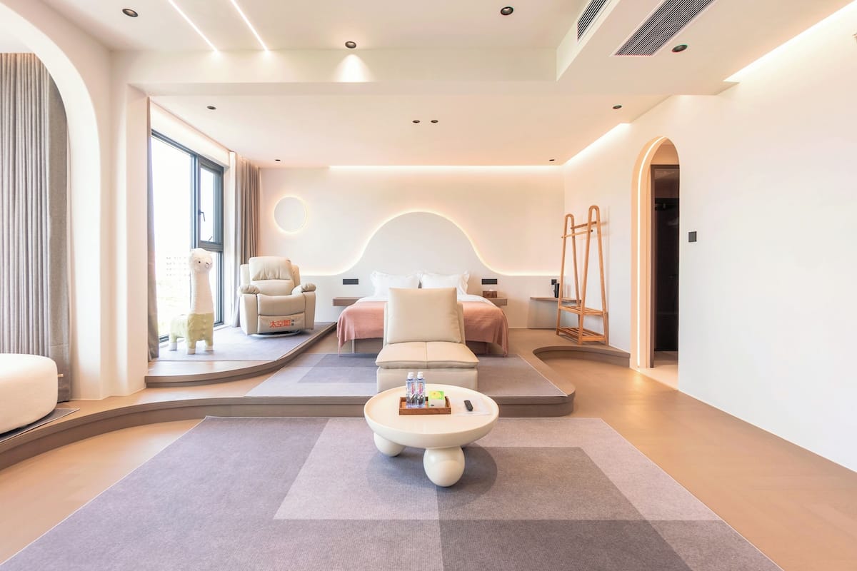 A modern hotel room with a sofa, a coffee table, a bed, and a large window.
