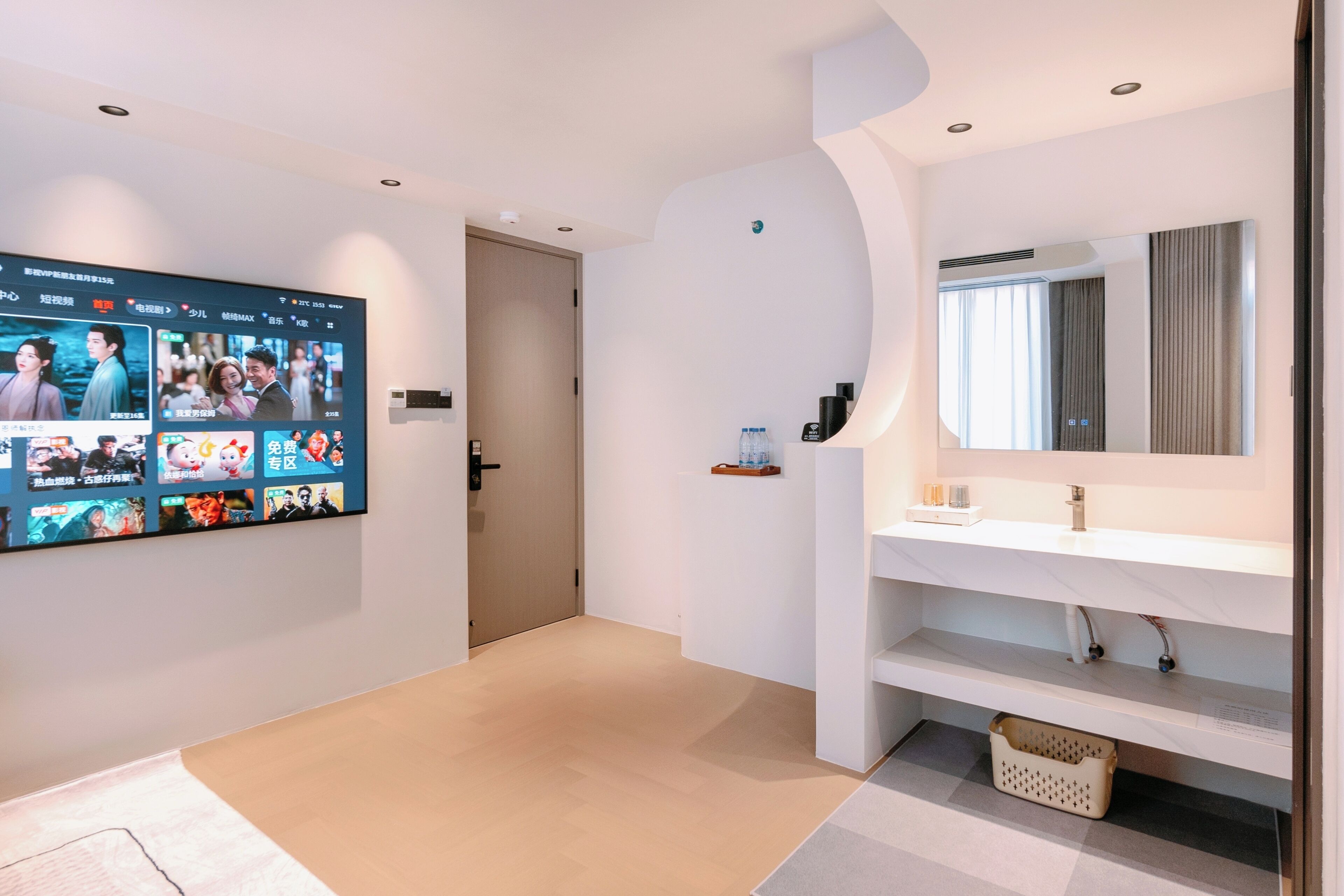 A modern hotel room with a large flat-screen TV displaying a movie, a white sink, and a mirror.