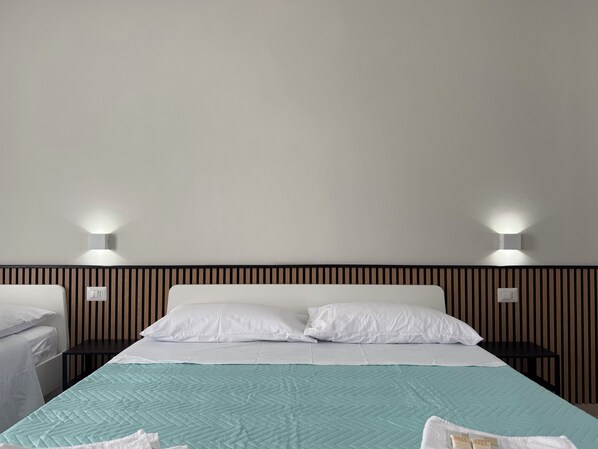 A neatly made bed with a teal quilt, two bedside tables, and wall-mounted lights.