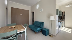 Un apartamento moderno con comedor, un sofá color turquesa, una kitchenette pequeña y un reloj visible en la pared.