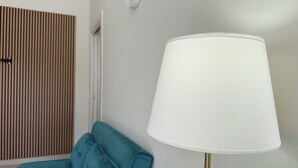 Una habitación con un sofá color turquesa, una lámpara blanca de base dorada y una puerta de listones de madera.