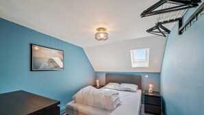 A bedroom with a bed, bedside tables, a hanging clothes rack, a framed picture, and a skylight.