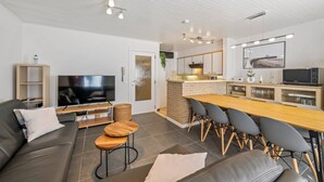 A modern living room with a sofa, TV, and dining area with chairs and a long table.