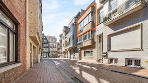 A narrow urban street lined with multi-story buildings, some with balconies and large windows.