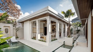 A modern outdoor pool area with a covered seating area, lounge chairs, and a clear view of the pool. - Villa Advaya (Kerobokan)